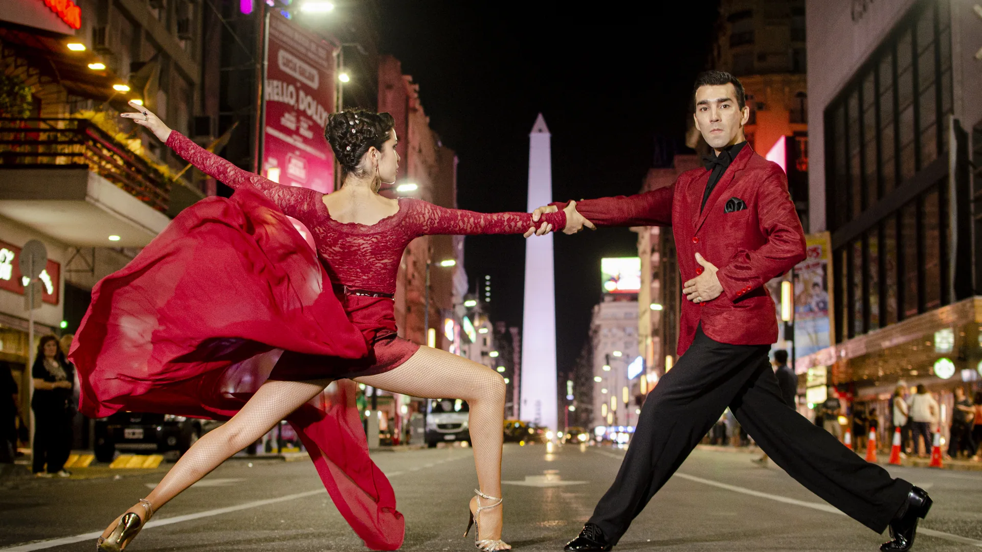 Two tango dancers in a dramatic pose on a Buenos Aires street at night, the woman in a flowing red dress, the Obelisco de Buenos Aires lit up in the background