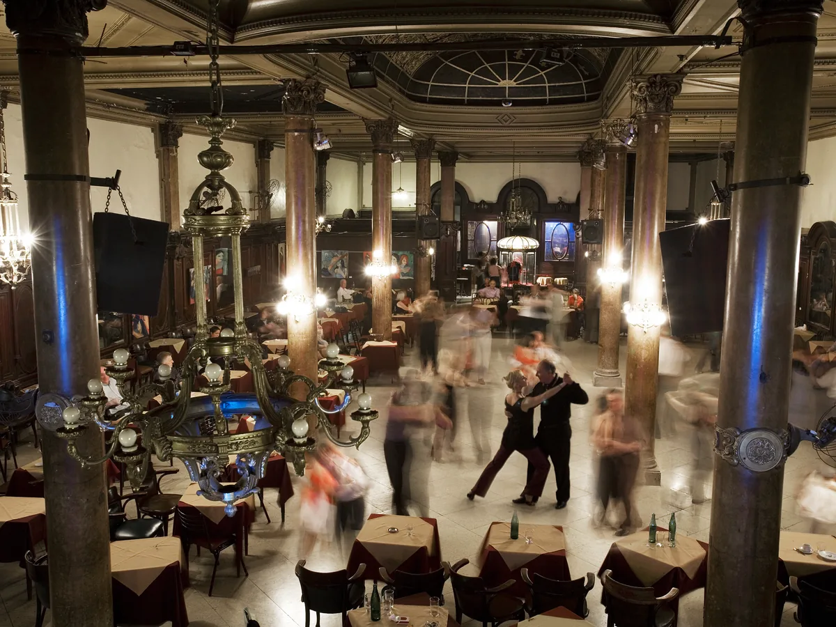 The ornate interior of Confitería La Ideal, a historic tango ballroom in central Buenos Aires, with columns, chandeliers and dancing couples on the floor